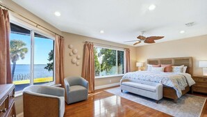 A bedroom with a large bed, a ceiling fan, a view of the sea, and a wooden floor. - Punta Gorda Harbor View Vacation Home - Waterfront Home with Private Pool (Punta Gorda)