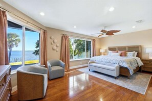 Une chambre dotée d’un grand lit, d’un ventilateur de plafond, d’une vue sur la mer et d’un plancher en bois.