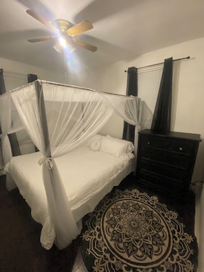 Ein Schlafzimmer mit Himmelbett, Deckenventilator, Kommode und einem gemusterten Teppich.