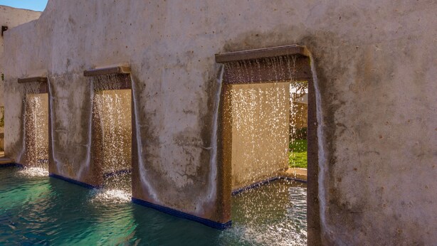 Une piscine dotée de jets d’eau jaillissant de ses bords, entourée d’un mur à la texture particulière.