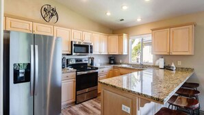 A modern kitchen with stainless steel appliances, wooden cabinets, a granite countertop, and a bar stool area. - Remodeled End Unit | Family Amenities | #609 (Saint George)