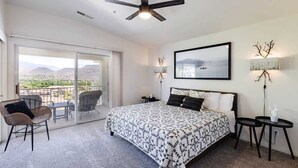 A bedroom with a bed, a ceiling fan, a balcony with chairs, and a view of the landscape. - Remodeled End Unit | Family Amenities | #609 (Saint George)