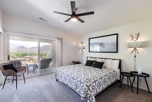 Ein Schlafzimmer mit einem Bett, Deckenventilator, einem Balkon mit Sitzgelegenheiten und Blick auf die Landschaft.