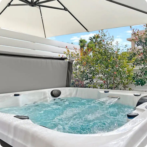 A hot tub with a white cover, surrounded by greenery and a clear sky.