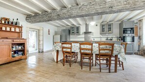 Een landelijke keuken met een hoog houten balkenplafond, een eettafel met bloemenlinnen en houten stoelen.