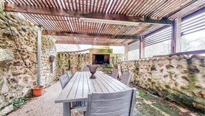 Een terras buiten met een houten tafel en stoelen, een stenen muur en een bakoven van baksteen.