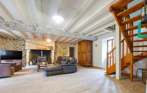 Ein geräumiges Wohnzimmer mit Kamin aus Stein, einer Ledersofa und einer Holztreppe.