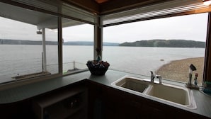 A kitchen with a large window overlooking a lake, a sink, and a countertop with a basket. - Anna's Bay Beach House, Union (Union)