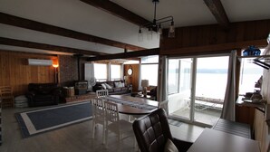 A spacious living area with a fireplace, dining table, and large windows offering a view of the water. - Anna's Bay Beach House, Union (Union)