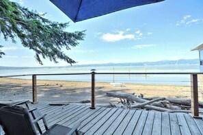 Une terrasse en bois avec une rambarde donnant sur une plage et l’océan.