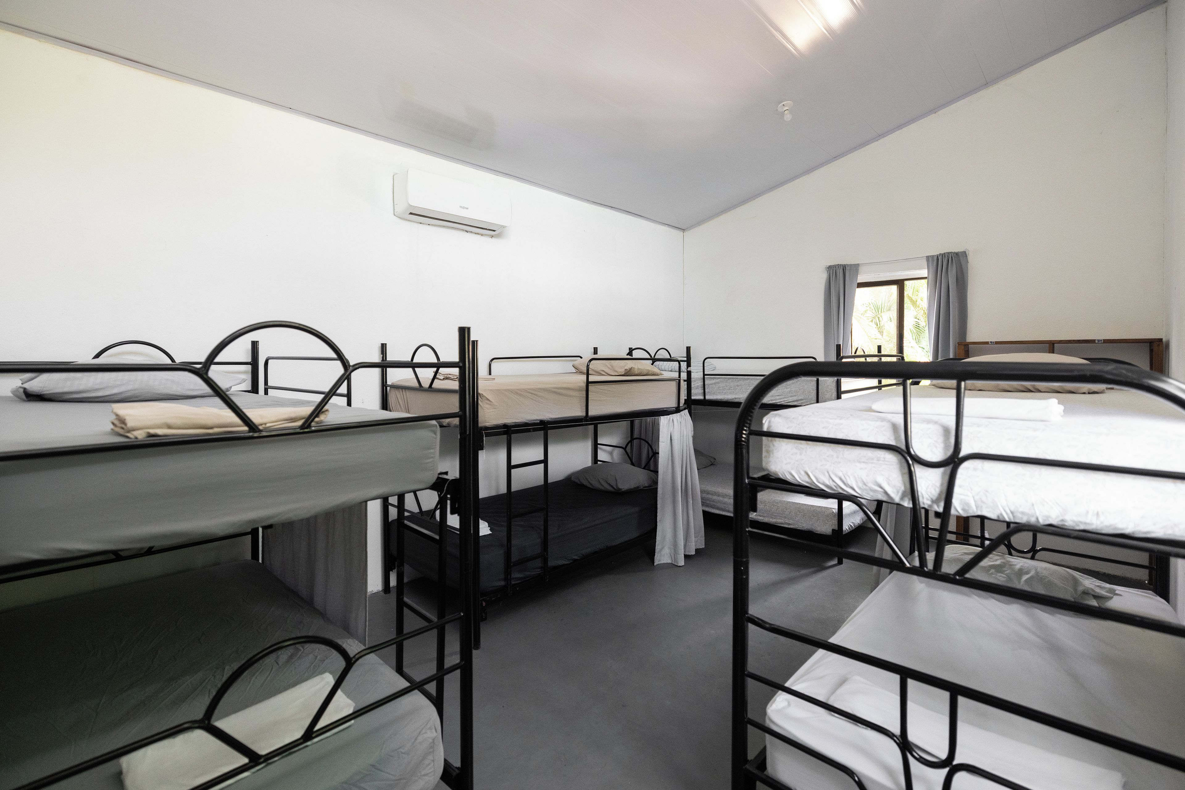 A dormitory room with bunk beds, a window with curtains, and an air conditioning unit.