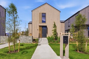 A modern two-story building with a concrete pathway leading to the entrance, surrounded by well-maintained grass and young trees. - Cynthia's Home away from Home (Queenstown)