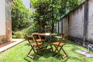A small outdoor seating area with a wooden table and chairs, surrounded by a grassy lawn and a stone wall. - Memora Guesthouse - Suite near Bacacheri Park (Curitiba)