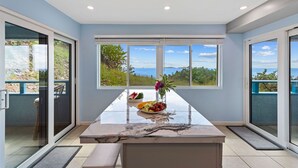 Eine moderne Küche mit Marmorarbeitsplatte, Obstschale und Blick auf das Meer durch große Fenster.
