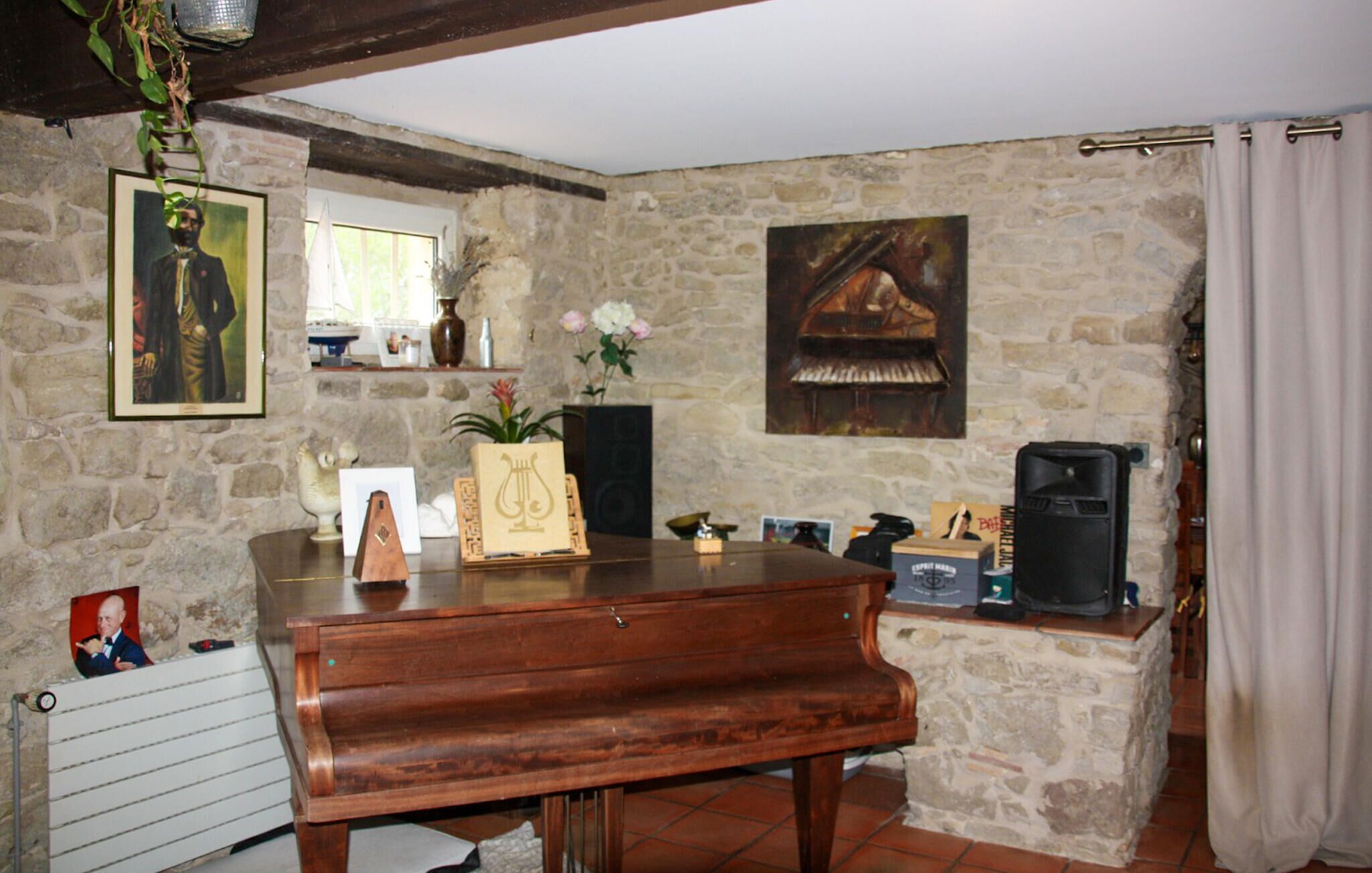 A rustic room with a piano, stone walls, a fireplace, and a window with curtains.