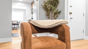 Een bruine fauteuil met een beige plaid in een kamer met houten vloer, een witte deur en een plant op de achtergrond.