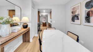 Een moderne keuken met houten kastjes, een marmeren aanrecht en een eethoek met een witte tafel en stoelen.
