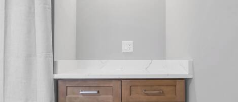 A bathroom with a white countertop, wooden cabinets, and a white wall.