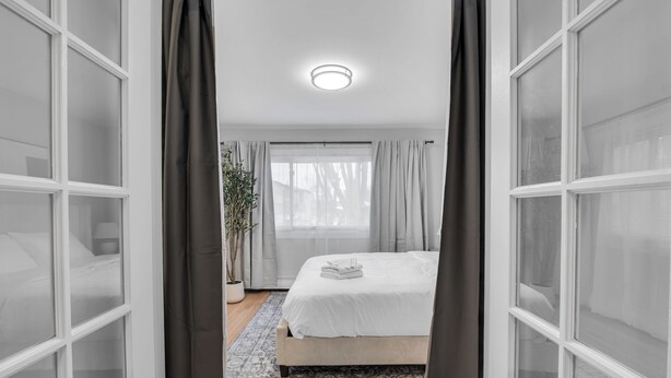 Een slaapkamer met een bed, gordijnen, een raam en een plafondlamp.