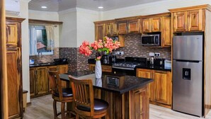 A modern kitchen with wooden cabinets, a stainless steel refrigerator, a microwave, and a central island with chairs. - Sy Villa (Choiseul)