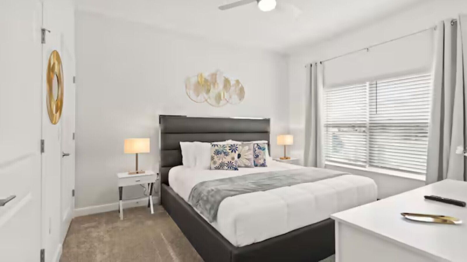 A modern bedroom with a bed, bedside tables, a desk, and a window with blinds.