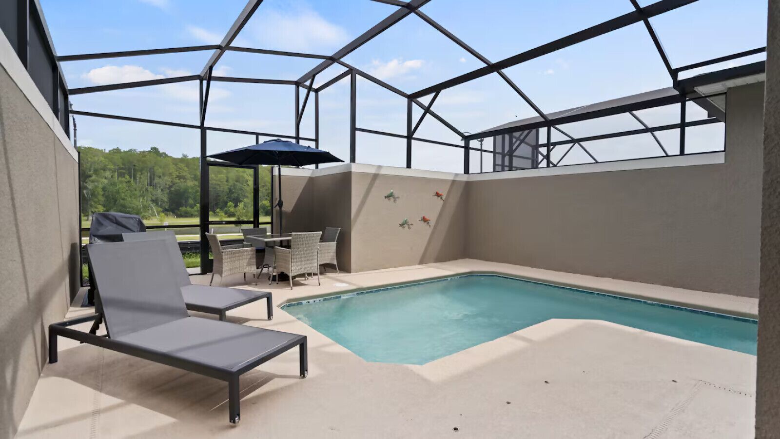 A covered outdoor swimming pool with lounge chairs and a table, surrounded by a glass enclosure.