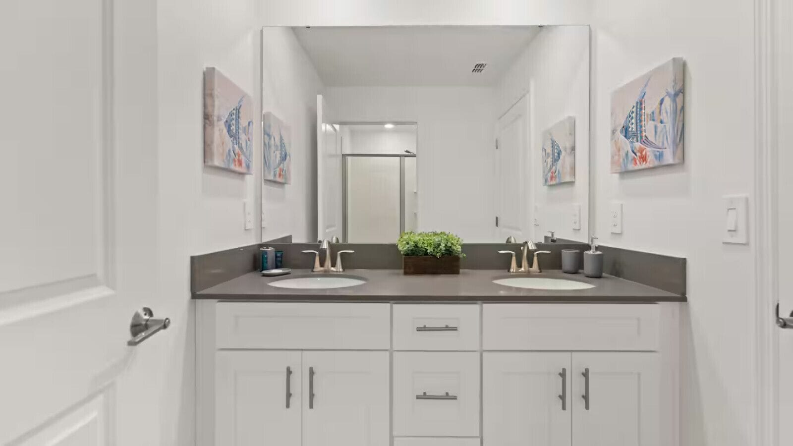Een moderne badkamer met twee wastafels, een grote spiegel en kunstwerken aan de muur.