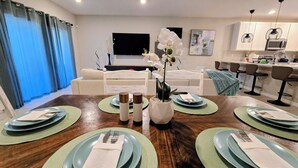 A dining area with a wooden table set for four, surrounded by a living room with a sofa and a TV. - Luxury Disney Home w/ Resort Pools, Tennis & Gym – Near Disney (Kissimmee)