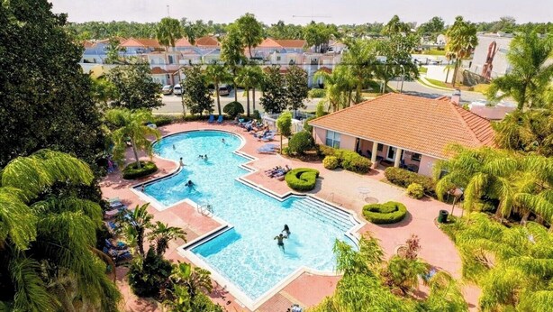 A large outdoor swimming pool surrounded by lush greenery and a building with a tiled roof. - Luxury Disney Home w/ Resort Pools, Tennis & Gym – Near Disney (Kissimmee)