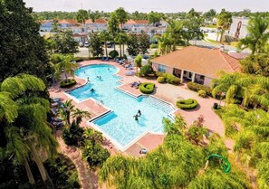 A large outdoor swimming pool surrounded by lush greenery and a building with a tiled roof. - Luxury Disney Home w/ Resort Pools, Tennis & Gym – Near Disney (Kissimmee)