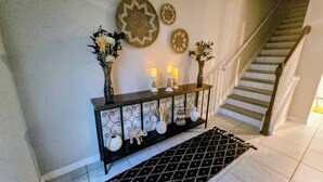 A staircase with a black and white patterned rug leading up to a dark wooden console table with decorative items and candles. - Luxury Disney Home w/ Resort Pools, Tennis & Gym – Near Disney (Kissimmee)