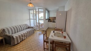 A cozy living area with a striped sofa, a dining table with chairs, and a kitchen in the background. - Lovely 2-room apartment for 4 people in Mt St Martin near the port of Cap d'Agde (LE CAP D AGDE)