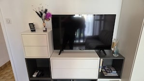 A modern living room with a flat-screen TV, a white cabinet, a small table with a remote control, and a decorative vase. - Lovely 2-room apartment for 4 people in Mt St Martin near the port of Cap d'Agde (LE CAP D AGDE)