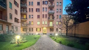 Ein mehrgeschossiges Wohngebäude mit zentralem Eingang, einem Steinweg und kleinen Gartenbereichen mit Beleuchtung.