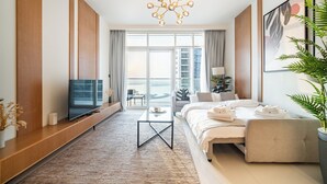 Una habitación de hotel moderna con una cama grande, televisión, mesa de centro y balcón con vistas.