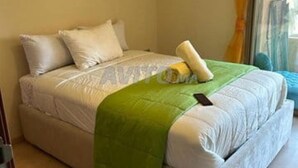 Ein Zimmer mit einem Einzelbett, einer grünen Decke, weißer Bettwäsche und einem Fenster mit Vorhängen.