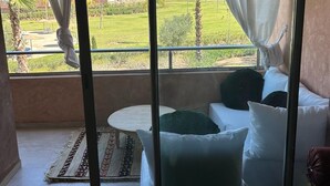 Ein Balkon mit Blick auf eine grüne Landschaft und Gebäude. Es steht eine weiße Couch mit grünen Kissen und ein kleiner runder Tisch darauf.