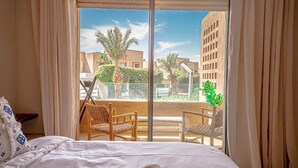 A hotel room with a large sliding glass door leading to a balcony with two wicker chairs and a potted plant. - Elegant Apartment with Panoramic View  (Marrakech)