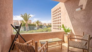 A balcony with a woven chair, a small table, and a potted plant.