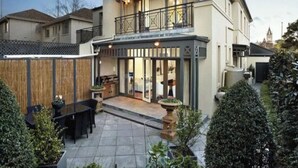 A two-story house with a balcony, a patio with outdoor furniture, and a garden area. - Luxurious Kew House - 5 min walk to cafes and restaurants (Kew)