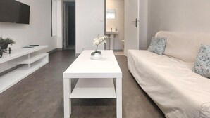 Ein modernes Wohnzimmer mit einem weißen Sofa, einem weißen Couchtisch und einem an der Wand montierten Fernseher.