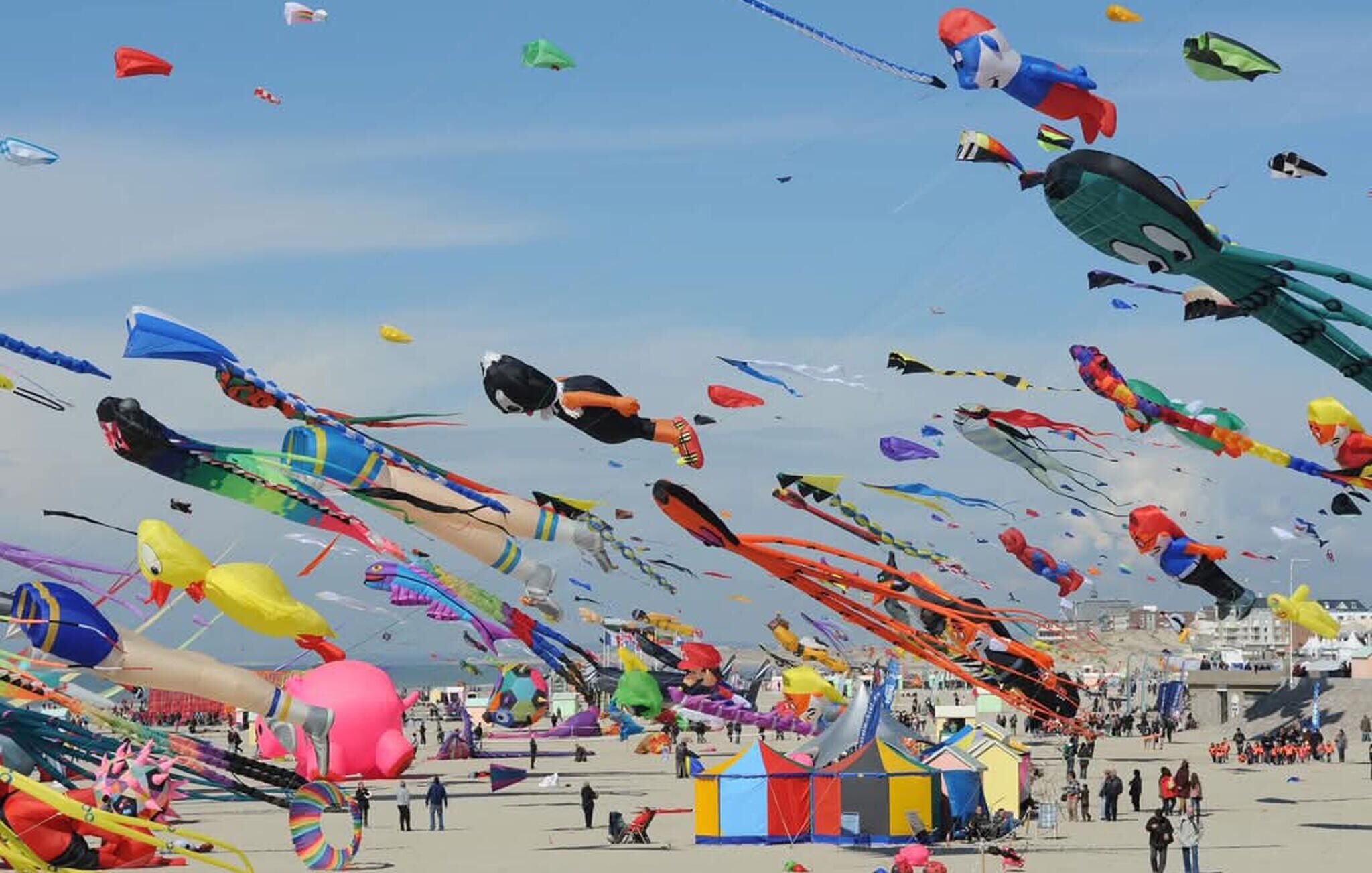 Une plage bondée où de nombreux cerfs-volants aux couleurs vives s’élèvent dans le ciel.