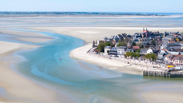Eine Küstenstadt mit Sandstrand, einem Steg und einer Mischung aus Wohn- und Geschäftsgebäuden.