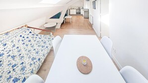Ein kompakter, moderner Raum mit Dachfenster, einer kleinen Küchenzeile und einem Essbereich mit Tisch und Stühlen.