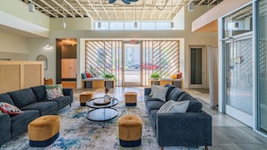A spacious lobby with modern furniture, a large ceiling fan, and a view of the street through large windows. - The Lotus Serene Stay with Pool-Gym-EV (Glendale)