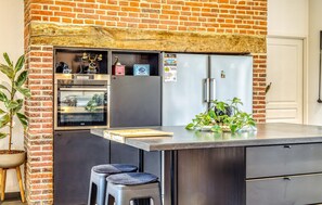 A compact kitchen with a brick wall, a built-in oven, a refrigerator, and a small bar stool. - Gorgeous home in Auvilliers with WiFi (Auvilliers)