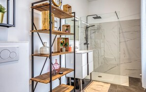 A bathroom with a glass shower enclosure, a white sink, and a wooden shelf unit with various items. - Gorgeous home in Auvilliers with WiFi (Auvilliers)
