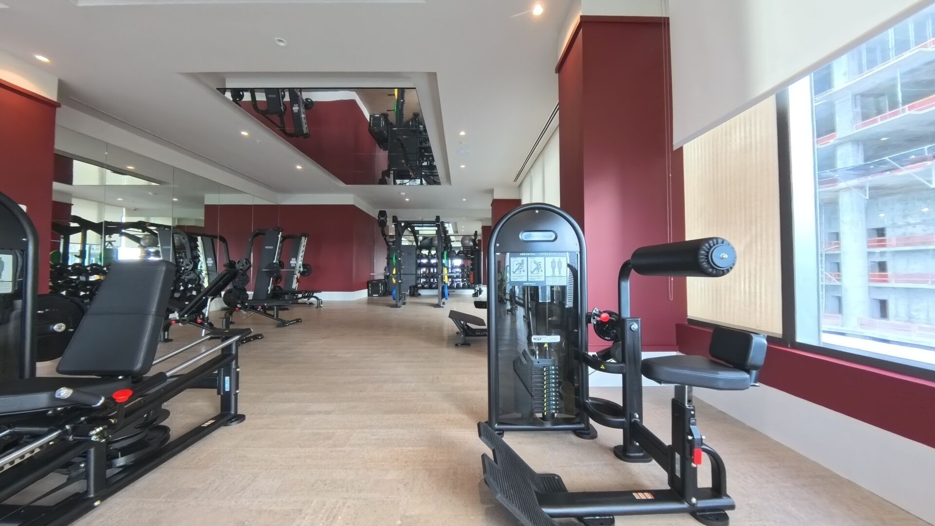 A gym with various exercise equipment, including treadmills and weight machines, with a large window on one side.