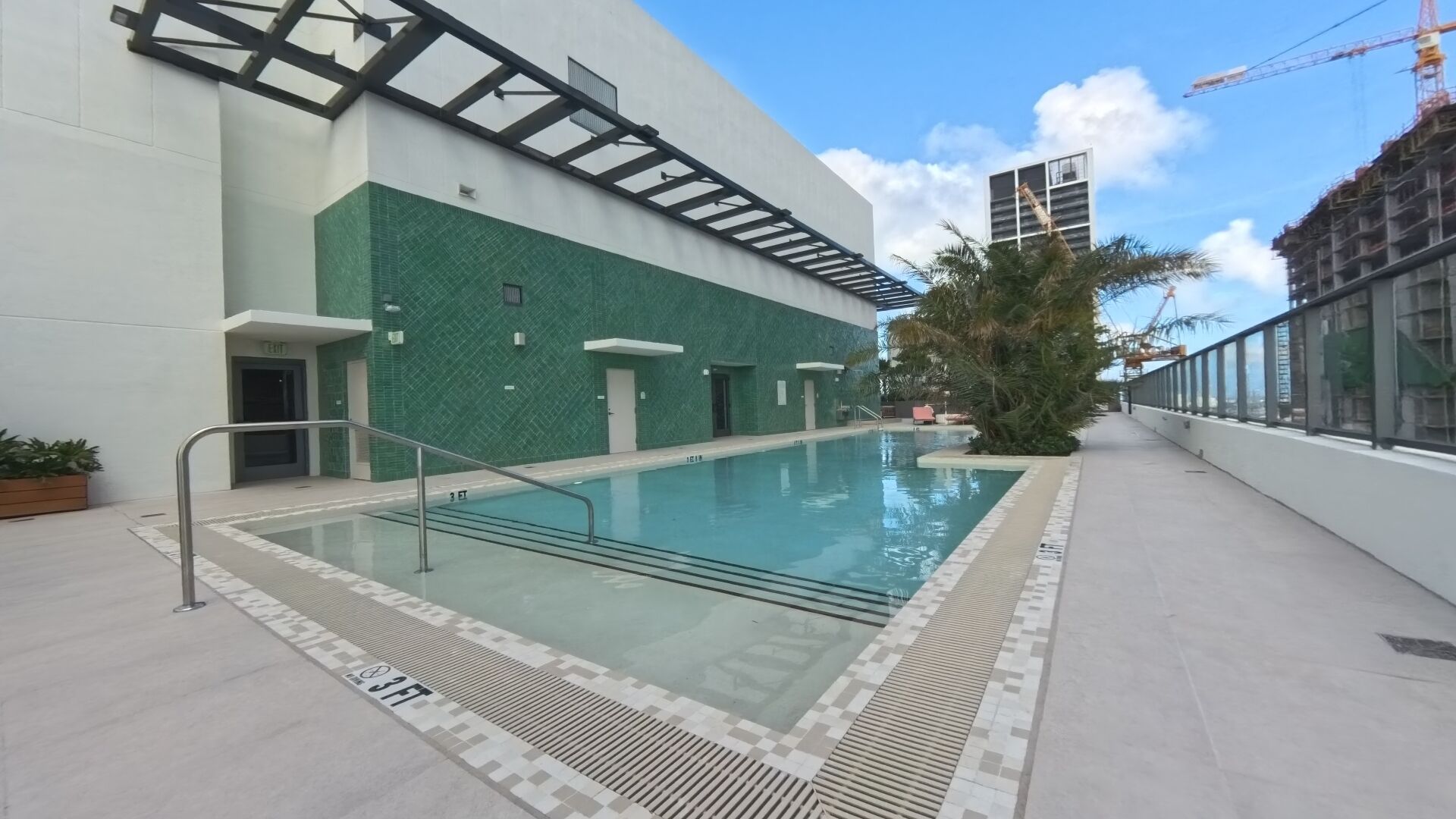 Ein moderner, überdachter Schwimmbereich mit klarem Wasser, umgeben von einer gefliesten Liegefläche und einer Glasbrüstung.