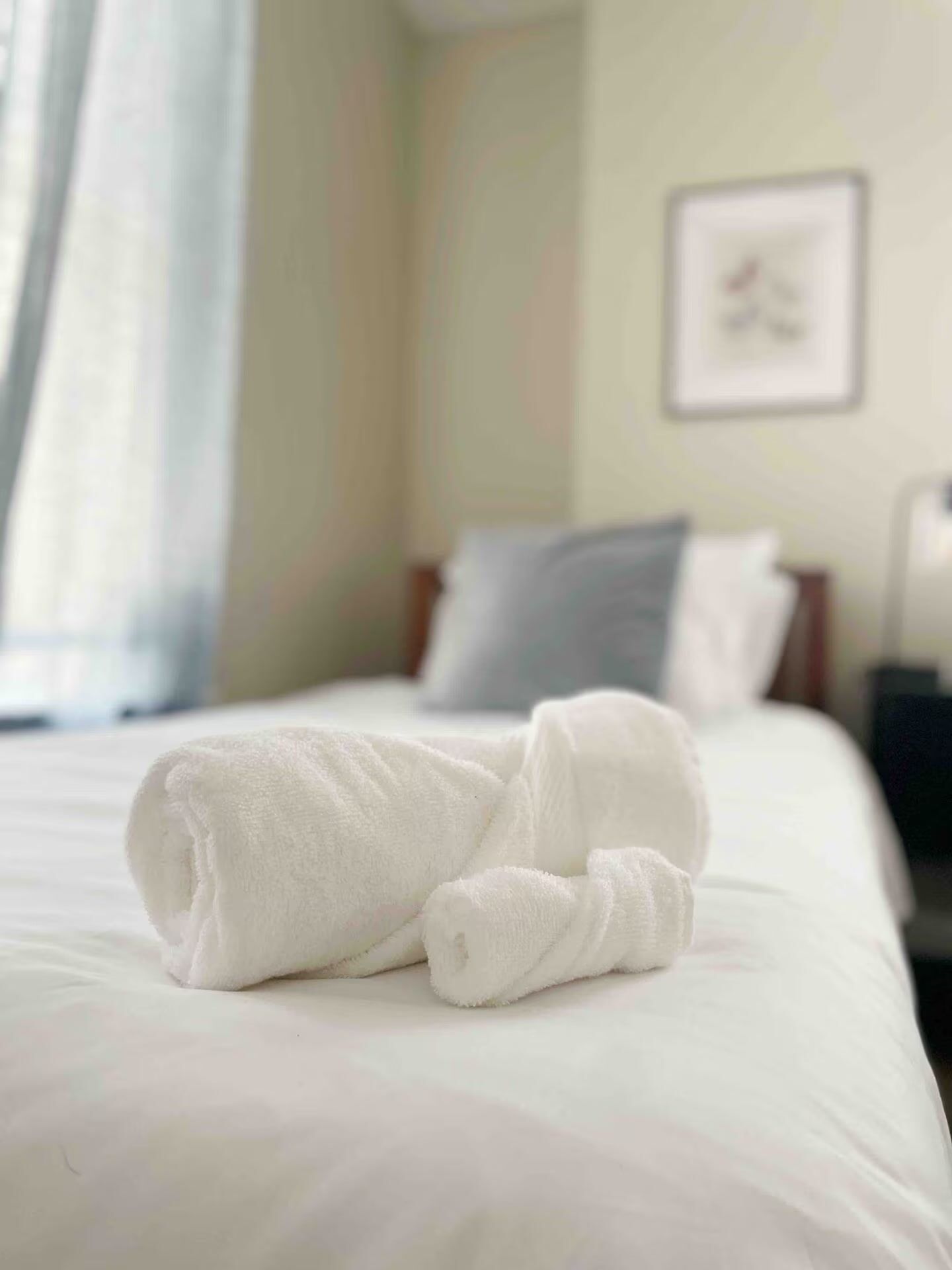 Een net opgemaakt bed met witte lakens en een opgerolde handdoek erop.